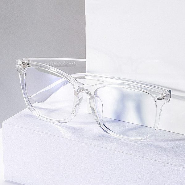 A pair of stylish blue light blocking glasses on a desk next to a computer and a phone.
